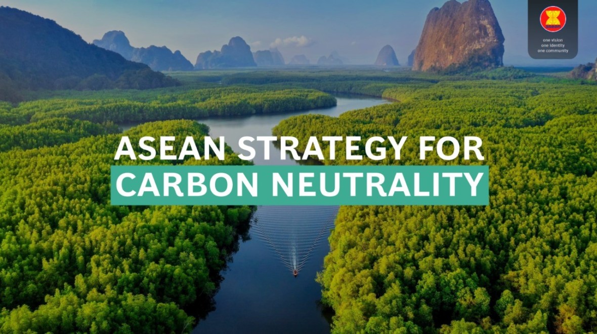 The photo captures a scenic view featuring a winding river with a small boat traveling down, surrounded by lush green trees. In the background, there is a prominent mountains covered in a blue mist. On the top right-hand side, the ASEAN logo is displayed, and in the center of the photo, the text reads 'ASEAN Strategy for Carbon Neutrality.' The image beautifully combines natural elements with a focus on environmental initiatives.