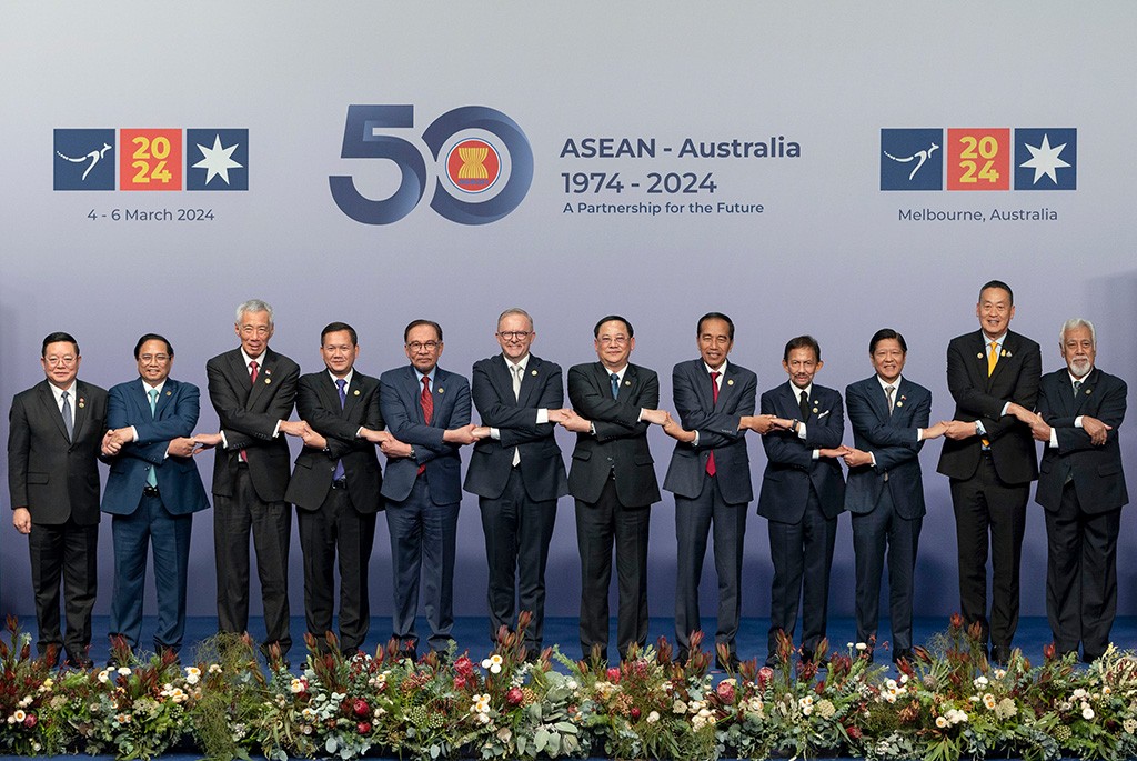 ASEAN leaders pose for the annual Family Photo during the ASEAN-Australia Special Summit 2024 in Melbourne.  They stand on stage in a crossed-arm formation, holding hands, with Australian native flowers in front. Behind them, the ASEAN "50" logo with the message" ASEAN-Australia 1974-2024 A partnership for the future", kangaroo icons, the year "2024," and the Australian Union star.”